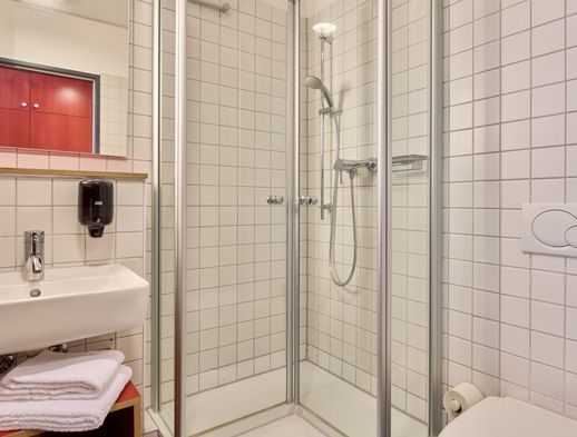 Helles Bad mit verglaster Dusche, Waschbecken, weißen Fliesen und gefalteten Handtüchern.