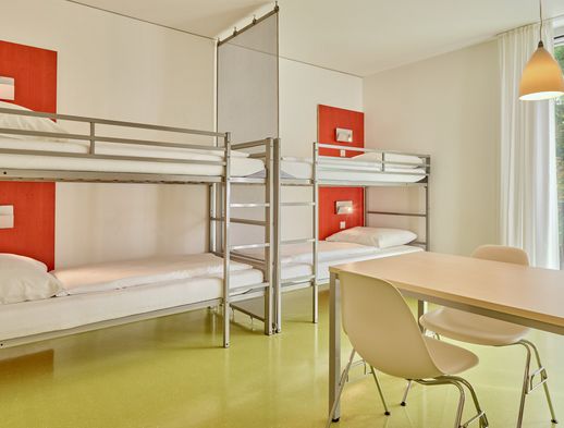 Helles Vierbettzimmer mit zwei Etagenbetten, Tisch, Stühlen und Fenster mit Blick ins Grüne